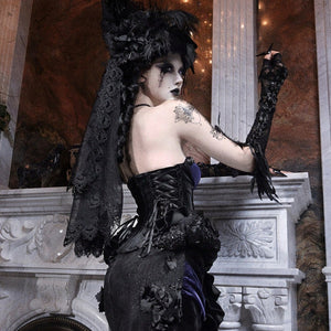 Back view of a model in a gothic black corset with lace overlay skirt, wearing a feathered hair piece.