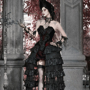 Full-body view of model in gothic corset bustier top, layered ruffled skirt with red brocade, hat, and garter stockings.