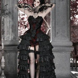 Model with arms raised in gothic black corset bustier top, red brocade, tiered ruffled skirt, and garter stockings.