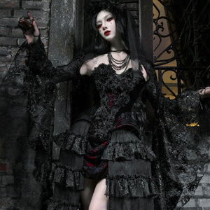 Gothic black velvet corset bustier top with sheer lace cape and tiered ruffled skirt, outdoors against stone wall backdrop.