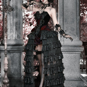 Model posing in a black gothic corset bustier top with red brocade accent and multi-tiered ruffled skirt, black stockings.