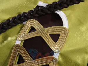 Genshin Impact Yaoyao cosplay top frames brown cut-out panel over lime green fabric beside gold coiled cord detail.