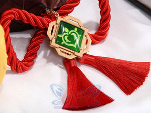 Genshin Impact Yaoyao cosplay pendant drops red cord and tassels beside gold-framed hexagonal green stone charm.