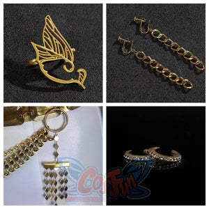 Displays four types of gold - colored accessories: a bird - shaped ring, chain clip - on earrings, a bag charm with layered chains and a pendant, and crystal - studded ear cuffs.