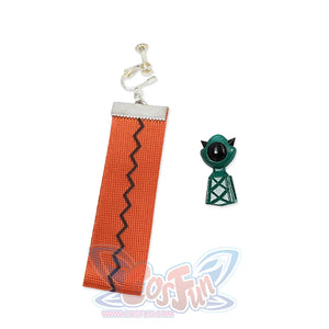 One orange webbing earring, one green earring with a black eye and pointed ears.