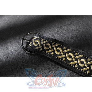 Close-up of a black strap with gold geometric embroidery and a round black metal buckle on suede fabric.