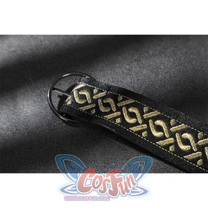 Close-up of a black strap with gold geometric embroidery and a round black metal buckle on suede fabric.
