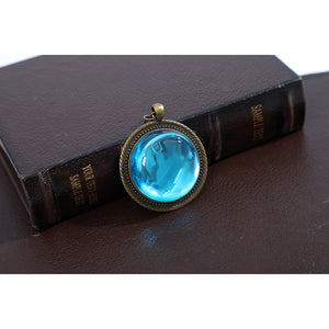 Wuthering Waves Denia cosplay gemstone pendant detail sets a bright blue oval inside an antique gold-tone frame.