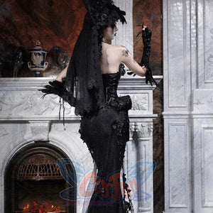 Back view of a model in a gothic black mermaid skirt with a long lace veil, standing near a marble fireplace.
