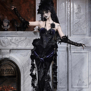 Model in a gothic black beaded corset with embroidered rose, feathered hat and long veil, arms extended outward.