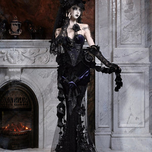 Model wearing a gothic black lace mermaid skirt and feathered hat, shown in a three-quarter pose by a fireplace.