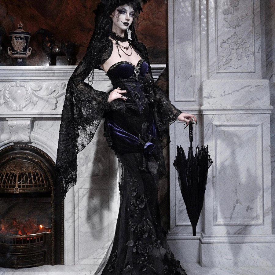 Model in a gothic black lace mermaid skirt with purple corset, holding a closed black umbrella by a fireplace.