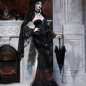 Model in a gothic black lace mermaid skirt with purple corset, holding a closed black umbrella by a fireplace.
