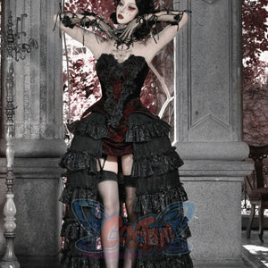 Model with arms raised in gothic black corset bustier top, red brocade, tiered ruffled skirt, and garter stockings.