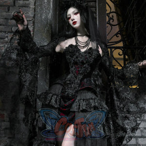 Gothic black velvet corset bustier top with sheer lace cape and tiered ruffled skirt, outdoors against stone wall backdrop.