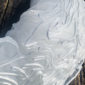Close-up of a white, textured fabric with wavy patterns on a wooden surface.