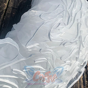 Close-up of a white, textured fabric with wavy patterns on a wooden surface.