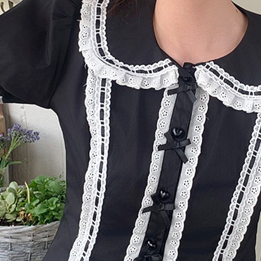Detail shot of black Lolita blouse showing white lace Peter Pan collar, eyelet trim, and black satin bows.