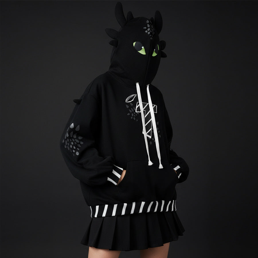 Person wearing a black hoodie with dragon design and skirt on a dark background