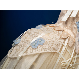 Enid Sinclair Gala dress side view with cream lace trim, blue floral appliques, ribbon bows, layered tulle ball gown skirt