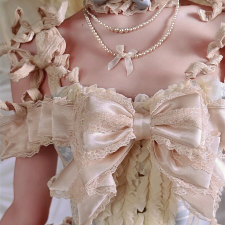 Close-up of cream bow, pearl trim, lace ruffles, and front button details