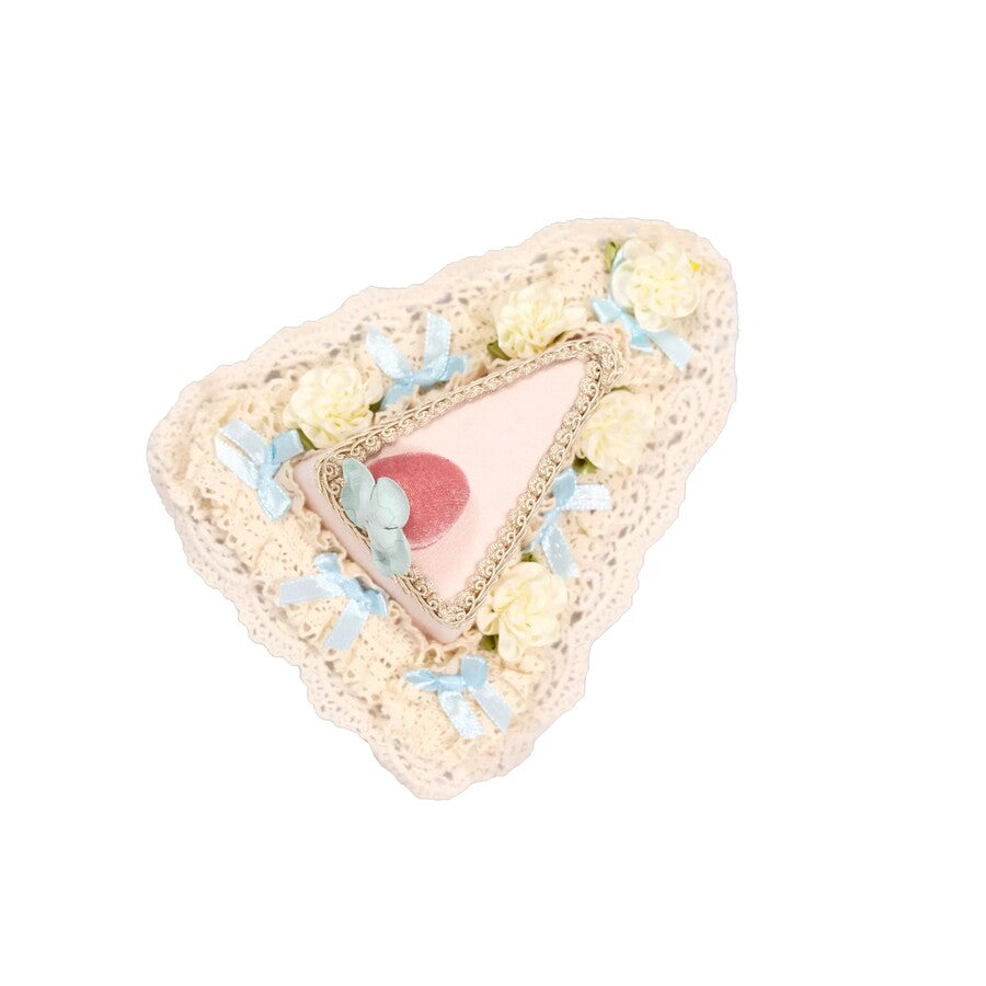 Cake-slice headpiece flat lay with cream lace, pale blue bows, and strawberry detail