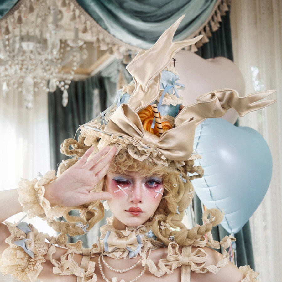 Dessert-themed headpiece worn with wing-shaped satin details and cake accents