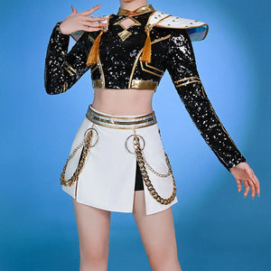 Zoey cosplayer wears black and gold sequin top with white skirt and gold chains on a blue background.