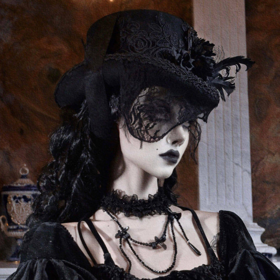 A model wearing a black Gothic Victorian flat-top hat with embroidered rose detail, black feathers, and a black lace veil, styled with a velvet gothic dress and layered necklaces