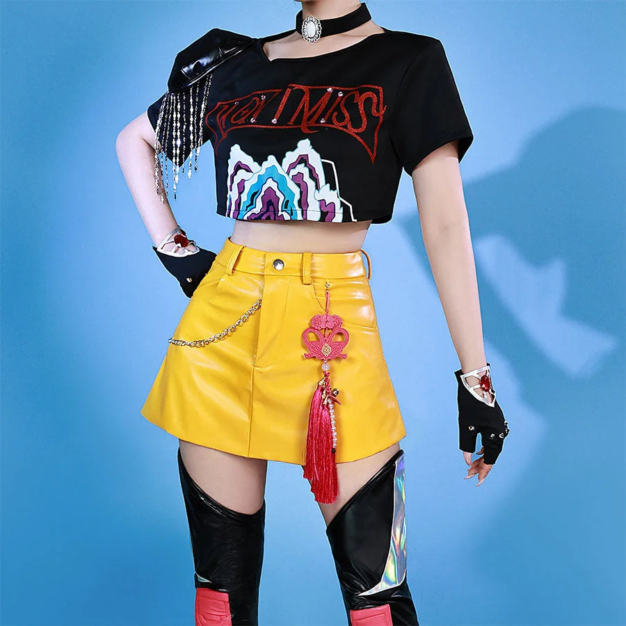 Idol Mira cosplayer wearing a black crop top with colorful graphics, yellow skirt, and black knee-high boots on a blue background