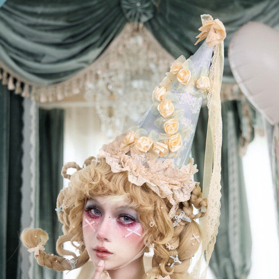 Cream pointed hat worn with rose trim, lace base, and long ribbon streamers