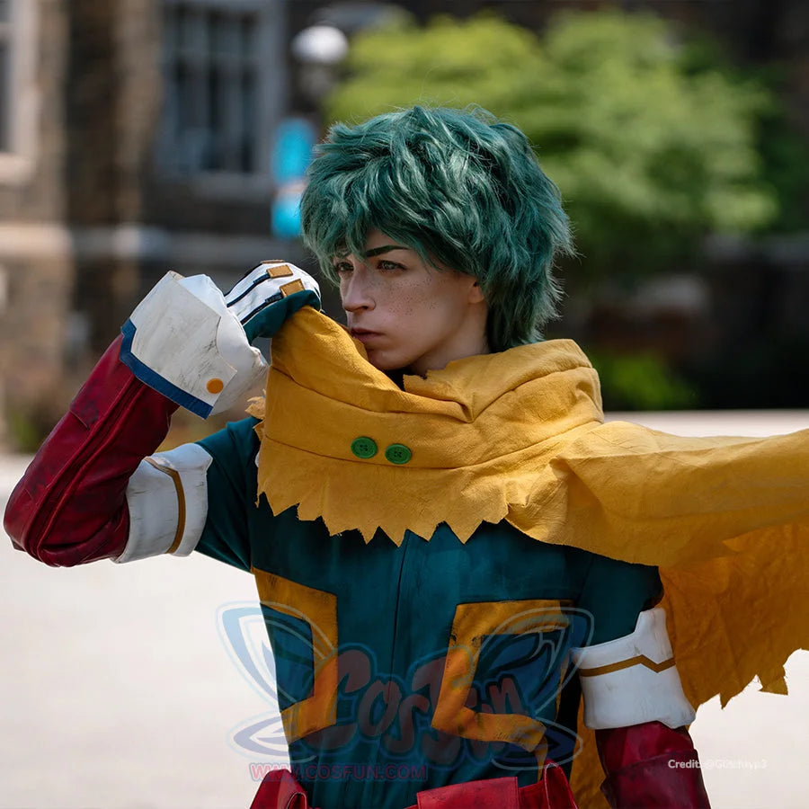 Deku cosplay costume upper-body close-up frames a yellow hooded cape over teal suit panels and a white wrist guard.
