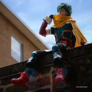 Deku cosplay costume seated view sets a yellow hooded cape above teal suit panels and black knee guards.
