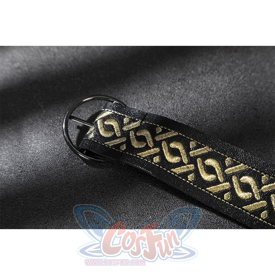 Close-up of a black strap with gold geometric embroidery and a round black metal buckle on suede fabric.