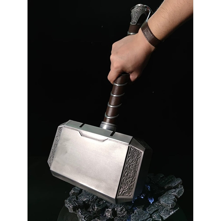 Thor cosplay hammer centers a rectangular metal block with ornate side carvings beneath a gripped cylindrical handle.